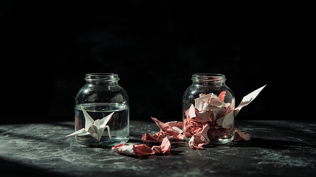 The Year-Two Bill That Kills Custom CRMs — illustration depicting Two glass jars on black slate: one pristine with a white paper crane in clear water, the other cracked and hemorrhaging crumpled red-inked invoices