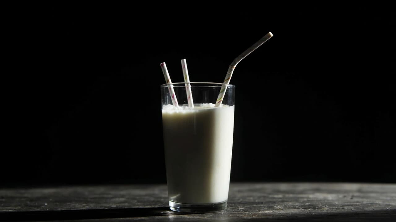 Your 'Dedicated' India Team Serves Three Clients — illustration depicting A single nearly drained glass of milk pierced by three bent drinking straws, the white liquid pooled at the bottom on dark wood
